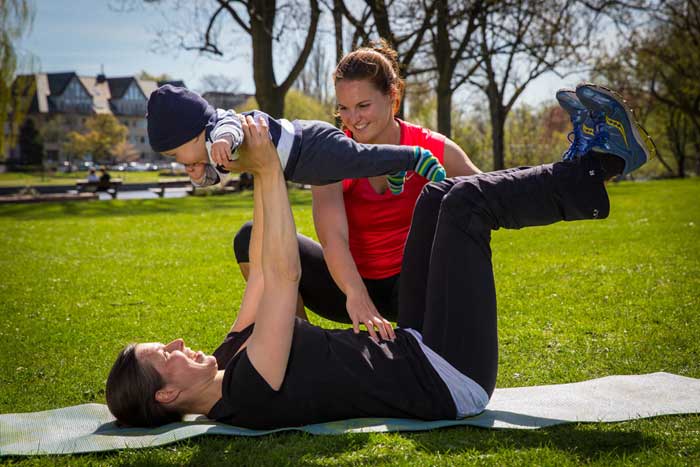 Mutter macht Sport hält ihr Baby und wird von Personal Trainerin angeleitet
