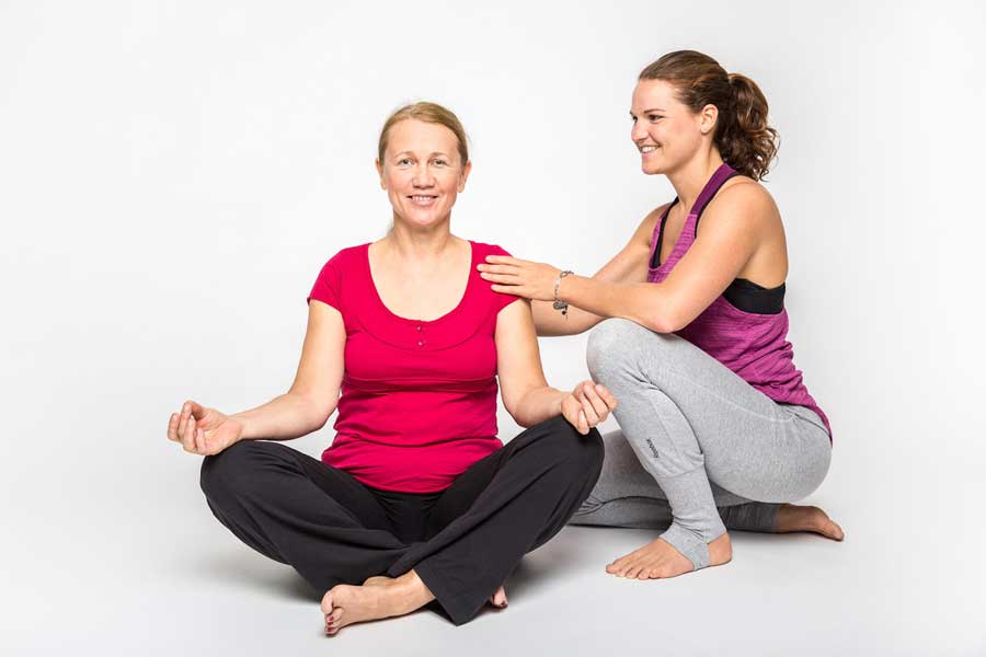 Ausführung einer Yoga-Übung mit Unterstützung eines Personal Trainers